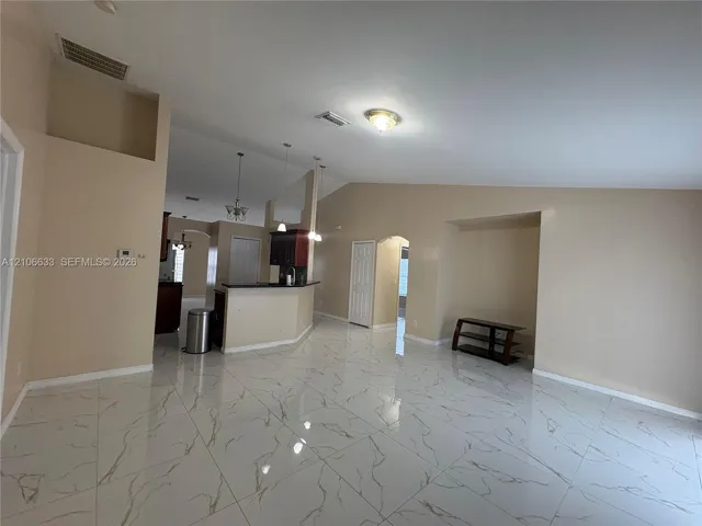 Open-concept interior featuring vaulted ceilings, polished large-format tile flooring, a kitchen peninsula, and recessed lighting