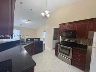 Kitchen featuring vaulted ceilings, cherry-finish cabinetry, dark solid-surface countertops, tile flooring, and stainless steel appliances
