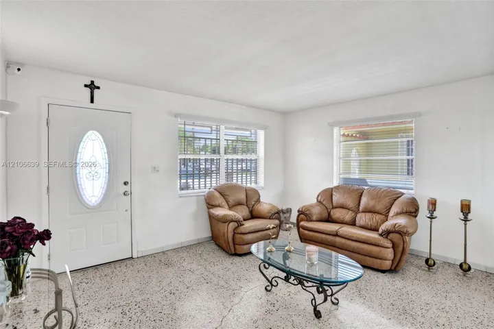 Interior space featuring polished terrazzo flooring, large windows with horizontal blinds, and a white entry door with an oval decorative glass insert