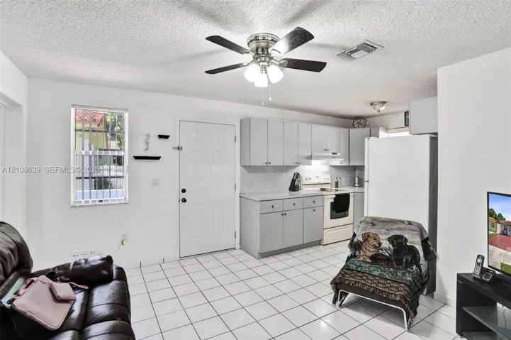 Kitchen featuring light gray cabinetry, solid surface countertops, tile flooring, a ceiling fan with integrated lighting, and a window with security bars