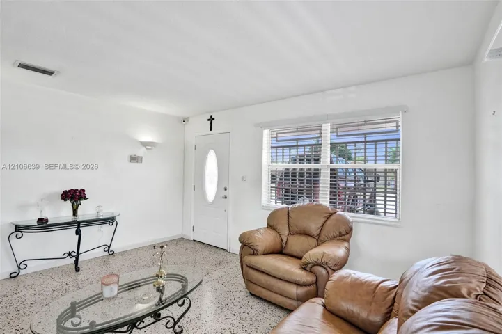 Living space featuring terrazzo flooring, white walls, and a recessed-panel entry door with an oval glass insert