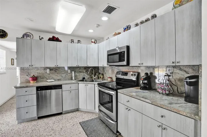 Kitchen featuring light-toned cabinetry, natural stone countertops with matching backsplash, stainless steel appliances, and integrated recessed lighting