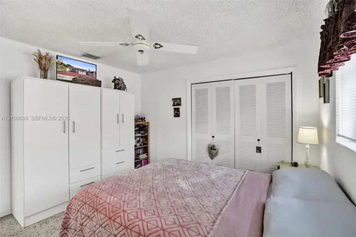 Room featuring built-in floor-to-ceiling cabinetry, dual louvered-door closet, overhead ceiling fan, and speckled-finish flooring