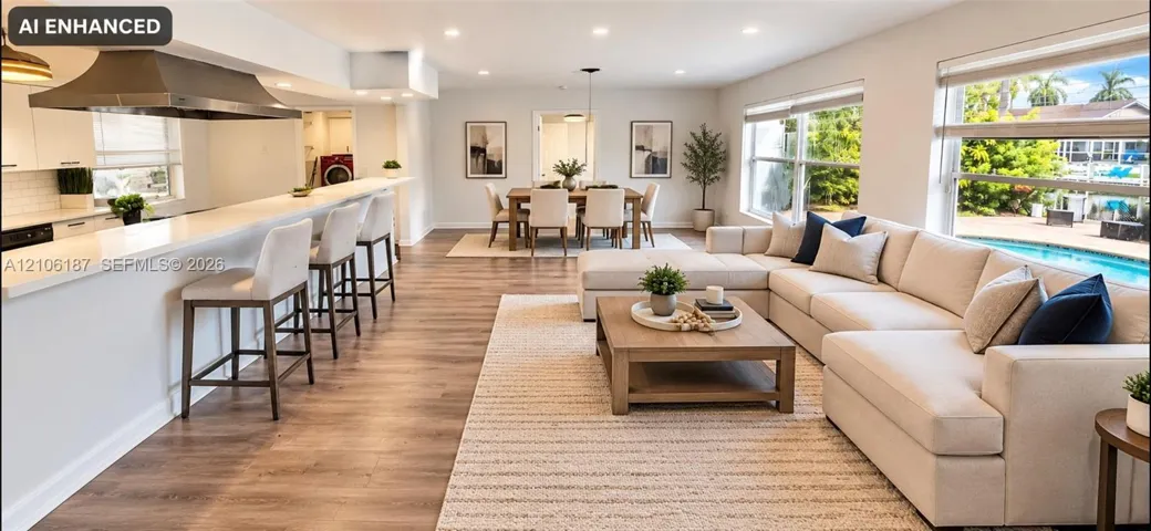 Open-concept living space featuring wood-finish flooring, recessed lighting, a breakfast bar with quartz countertop, and a stainless steel range hood