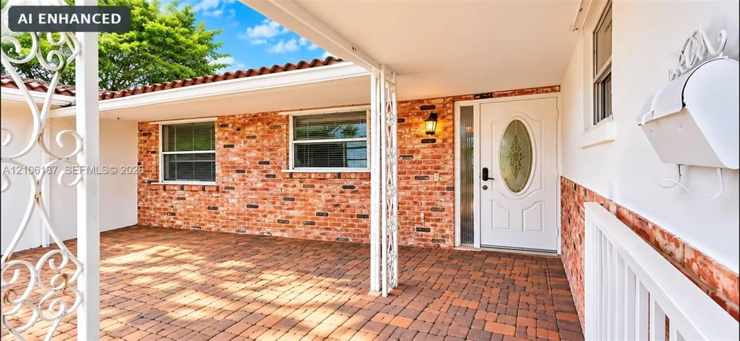 Covered front entry featuring red brick exterior siding, terracotta-style roof tiles, decorative metal porch supports, and a paved brick porch