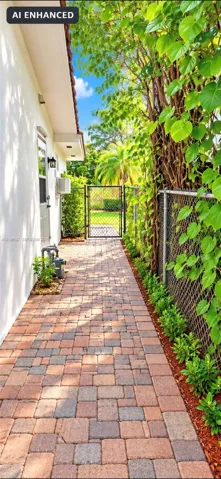 Side yard featuring a multi-tone paver walkway, metal chain-link fencing, a metal gate, and exterior wall-mounted lighting