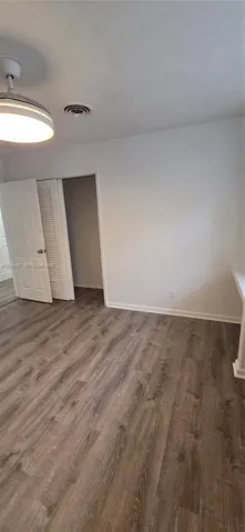 Interior space featuring wood-finish flooring, a neutral color palette, built-in closet with louvered doors, and a central ceiling-mounted light fixture