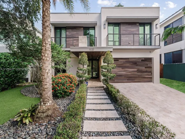 Contemporary two-story exterior featuring smooth stucco facade, horizontal wood-finish cladding, second-story balcony with metal railing, and paver walkway set in stone aggregate