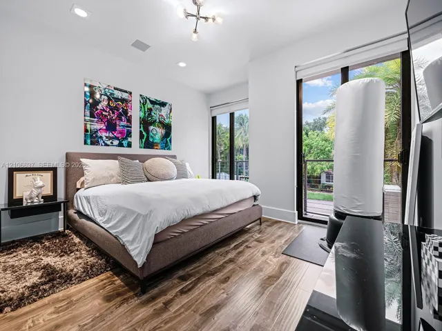 Wood-finish flooring, recessed lighting, modern multi-arm ceiling fixture, and floor-to-ceiling glass sliding doors opening to an outdoor balcony
