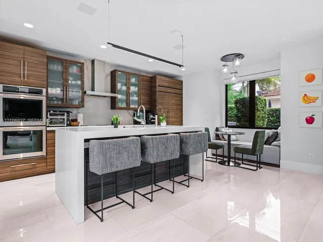 Modern kitchen featuring horizontal-grain wood cabinetry, a central island with a waterfall-edge countertop, built-in double wall ovens, recessed lighting, and large-format tile flooring