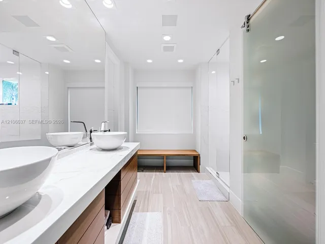 Floating vanity featuring dual vessel sinks, stone-finish countertops, wood-grain cabinetry, and a sliding glass door entry to a walk-in shower