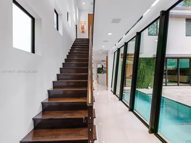 Staircase featuring dark wood treads and a linear handrail, large-format tile flooring, recessed ceiling lighting, and floor-to-ceiling glass wall panels overlooking a pool