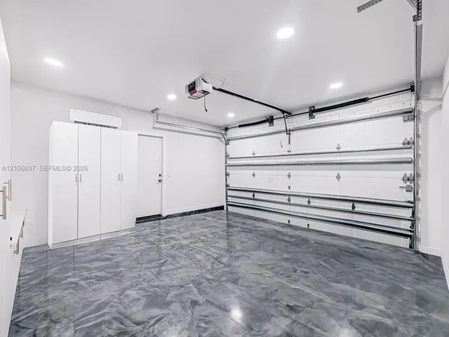Garage featuring high-gloss epoxy flooring, built-in white cabinetry, recessed LED lighting, and a climate control unit