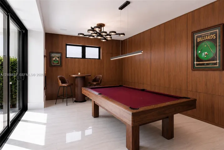 Wood-paneled walls, large-format tile flooring, multi-light modern chandelier, horizontal linear pendant light, and black-framed sliding glass doors