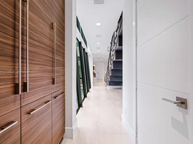 Hallway featuring wood-finish cabinetry with vertical hardware, large-format tile flooring, recessed ceiling lighting, and a dark-toned staircase with metal handrails
