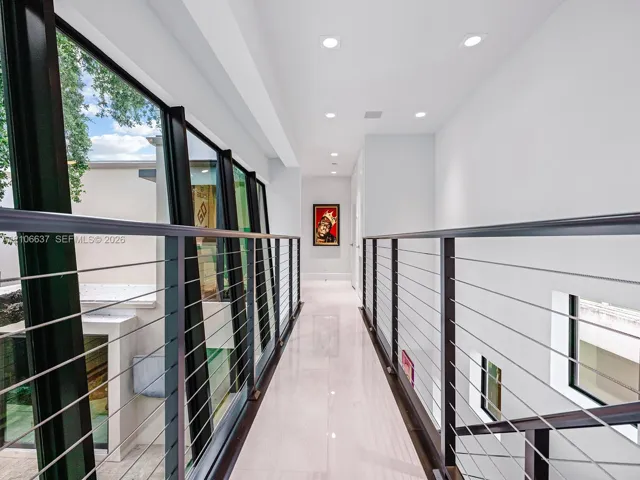 Hallway featuring polished light-toned flooring, recessed ceiling lighting, and a metal cable railing system with dark-finish posts, complemented by floor-to-ceiling glass paneling