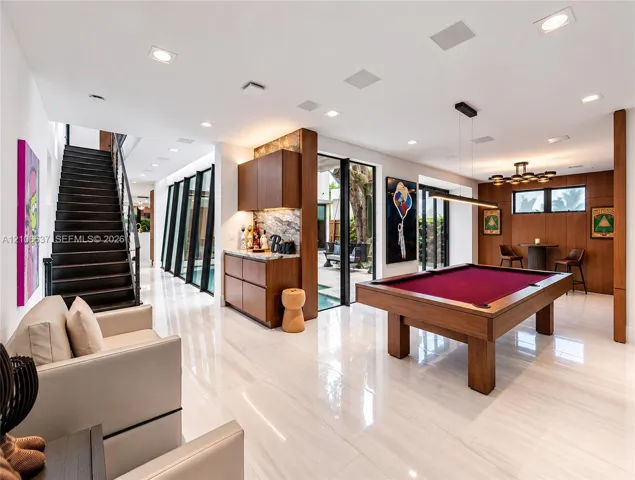 Polished stone flooring, wood-panelled accent walls, integrated bar cabinetry with stone backsplash, staircase with open risers, and floor-to-ceiling glass paneling