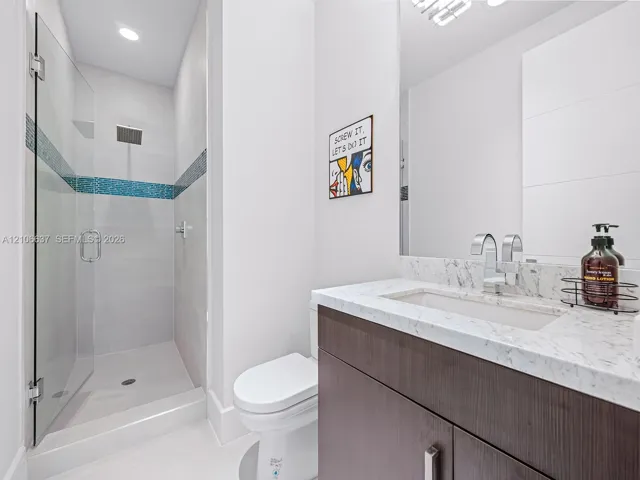 Modern bathroom featuring a dark wood-finish vanity, light-toned stone-finish countertop with an integrated rectangular sink, glass-enclosed shower with decorative tile inlay, and chrome fixtures
