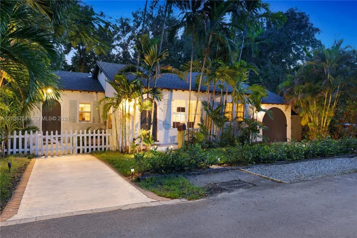 Stucco exterior featuring dual arched entryways, a white picket fence, concrete driveway, and mature palm landscaping