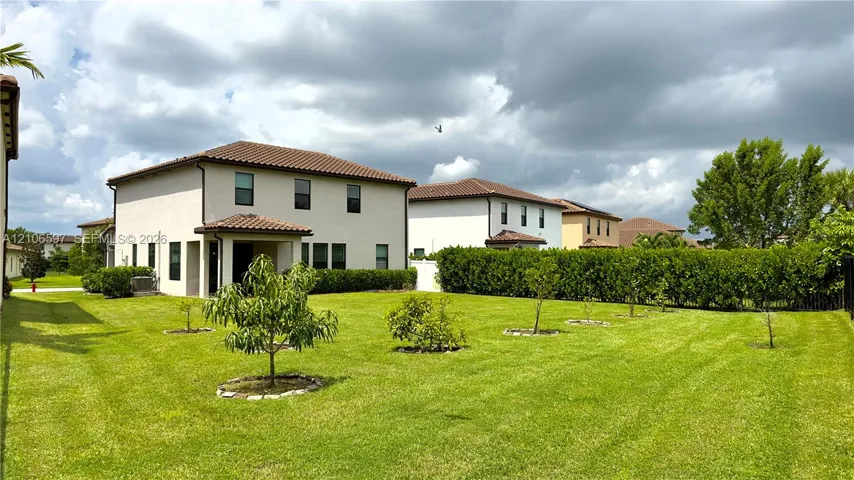 Expansive backyard featuring a manicured lawn, established perimeter hedge, and young trees