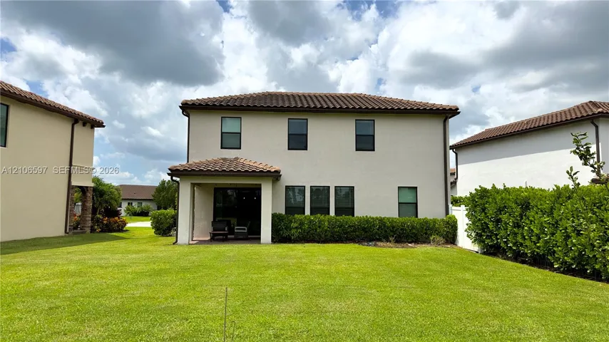Two-story exterior featuring a tile roof, stucco finish, covered patio, and manicured lawn with privacy hedging