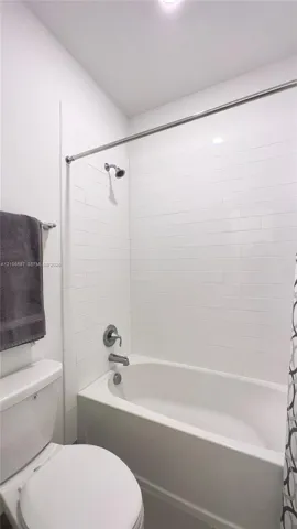 Upstairs guest bathroom Full-size bathtub featuring white subway-style wall tiling, a wall-mounted shower head, and a chrome-finish diverter faucet