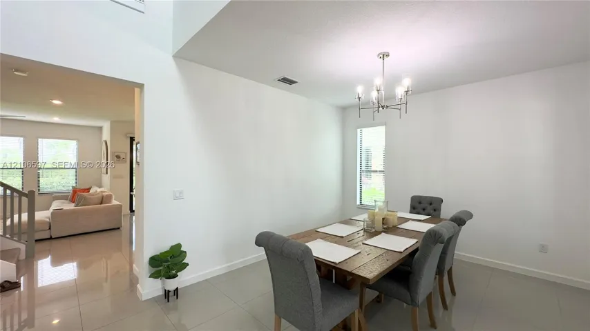 Open-concept dining area featuring high ceilings, neutral tile flooring, and a multi-arm chandelier