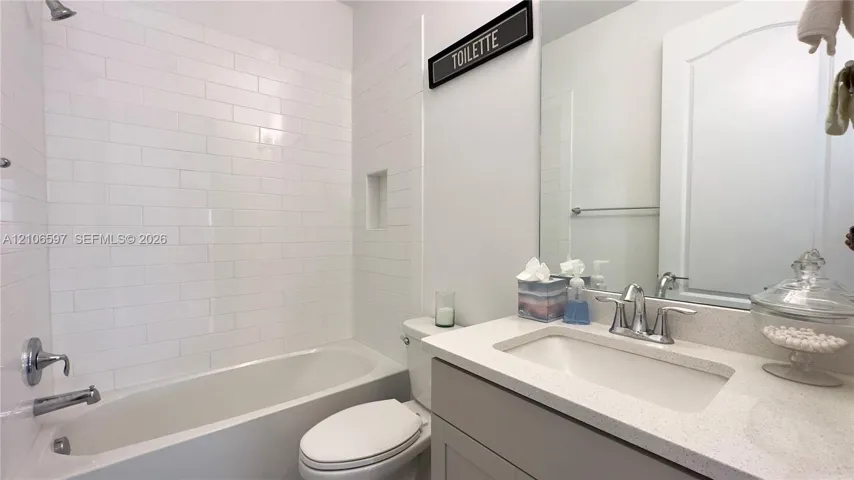 First floor guest Bathroom featuring a white subway tile shower surround, integrated wall niche, quartz countertop, and vanity cabinet with an undermount sink