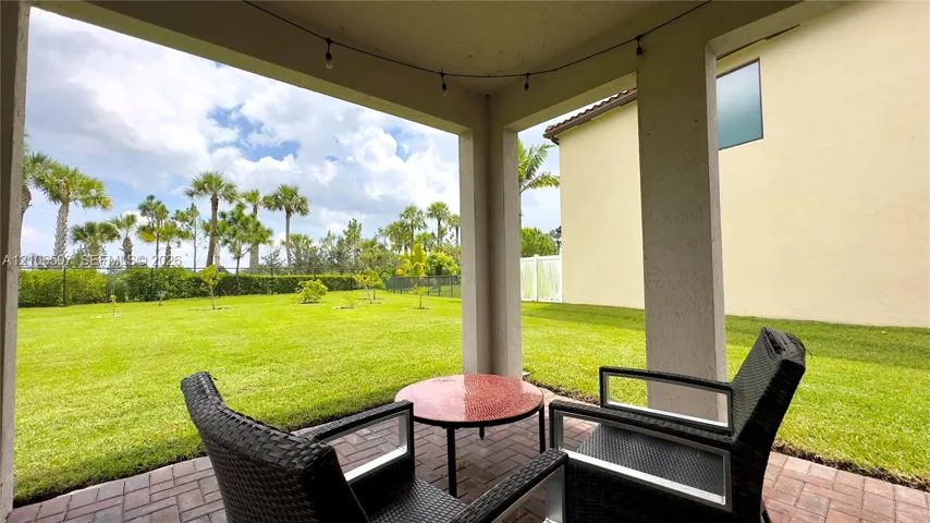Covered patio featuring brick pavers and a sprawling lawn with mature palm trees