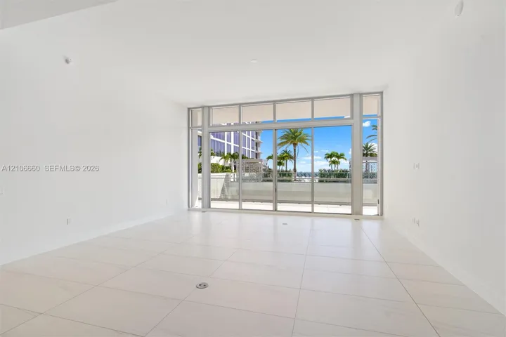 Open-concept interior featuring large-format tile flooring, floor-to-ceiling glass wall, and sliding glass doors leading to an exterior balcony
