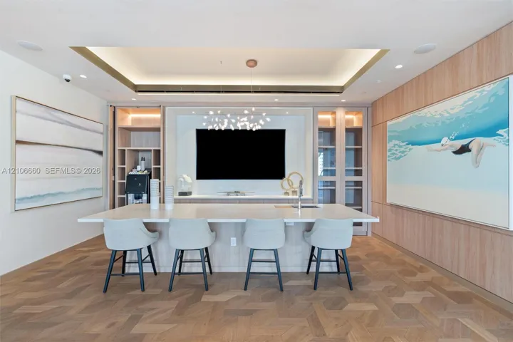 Custom millwork wall unit with built-in cabinetry and display shelving, integrated wet bar with sink, tiered tray ceiling with recessed lighting, and herringbone-pattern wood-finish flooring