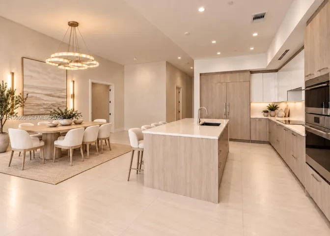 Kitchen featuring light wood-finish cabinetry, a large central island with light-toned countertops, integrated stainless steel appliances, recessed lighting, and a multi-tiered circular chandelier
