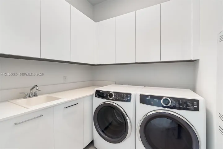 Laundry area featuring high-gloss white upper and lower cabinetry, solid surface countertop, and an integrated basin with a chrome faucet