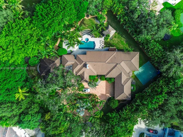 Aerial perspective of a sprawling property featuring a paved circular driveway, a swimming pool with spa, a tennis court, and mature perimeter landscaping