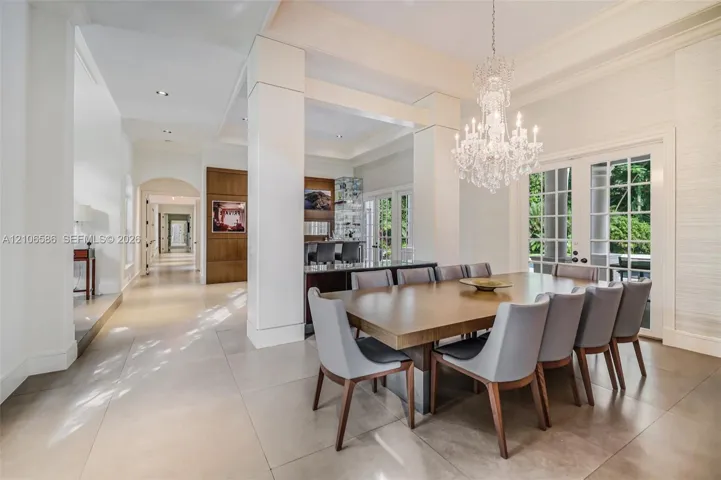 Spacious dining area featuring large-format tile flooring, tray ceilings, floor-to-ceiling columns, a crystal chandelier, and French door access to the exterior