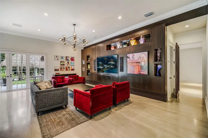 Custom wood-veneer accent wall featuring integrated recessed shelving, multi-arm geometric chandelier, light-toned flooring, and floor-to-ceiling glass-paneled double doors