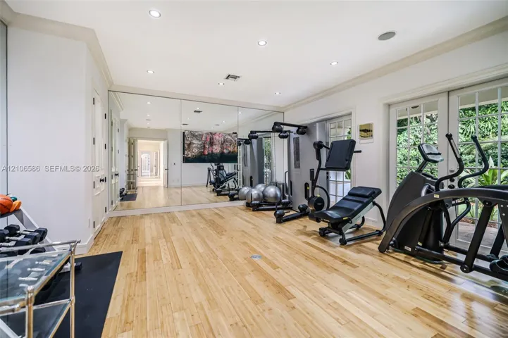 Room featuring wood-finish flooring, recessed lighting, expansive wall-to-wall mirrors, and dual sets of glass-paneled french doors