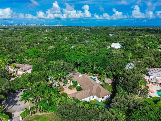 Aerial perspective featuring a multi-gabled roofline, a circular paved driveway, a private swimming pool, and extensive mature landscaping on a heavily wooded lot