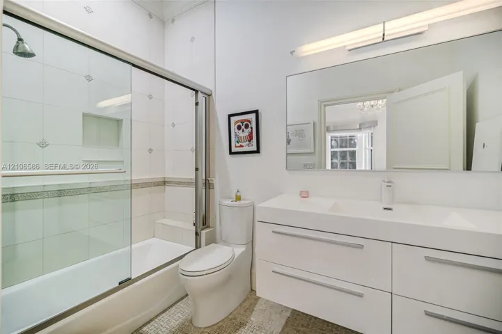 Modern bathroom featuring a high-gloss double vanity with an integrated countertop, large-format tiled walls with decorative inlay, built-in shower niche, glass shower enclosure, and linear wall-mounted lighting