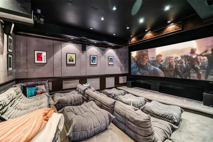 Media room featuring tiered flooring, custom wall paneling, crown molding, and recessed lighting