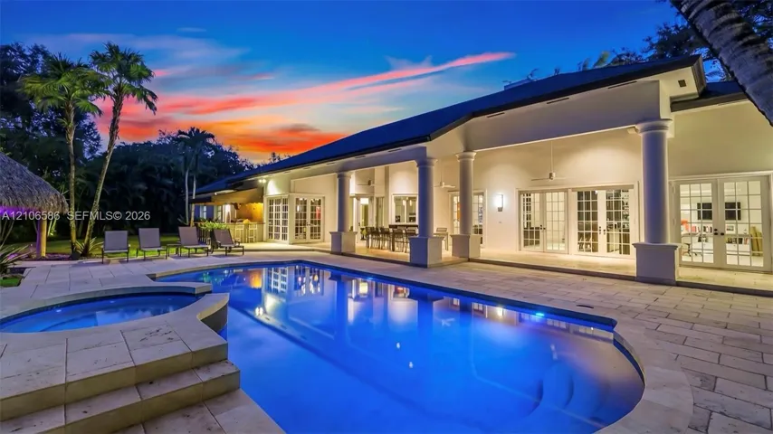 Spacious exterior featuring a covered patio with columns, stone-paved decking, a built-in swimming pool, a separate spa, and multiple sets of French doors
