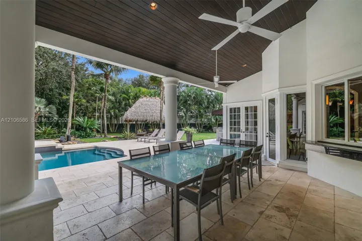 Covered patio featuring stone-tile flooring, a wood-paneled ceiling, ceiling fans, and structural columns