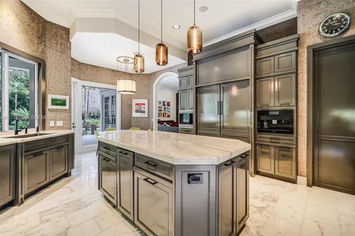 Custom cabinetry with panel-ready integrated appliances, expansive stone-topped central island, polished stone flooring, and multi-pendant lighting