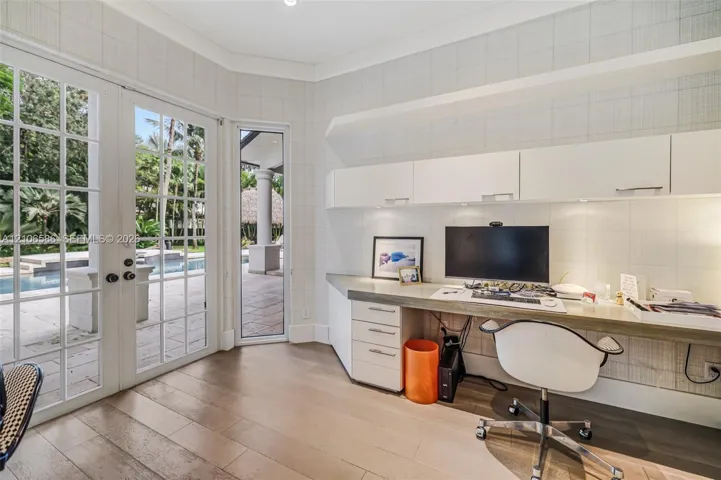 Custom built-in desk with integrated storage cabinetry, wood-finish flooring, and white paneled walls featuring multi-pane glass doors