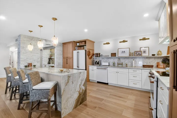 Kitchen featuring a stone-topped waterfall island, custom white cabinetry, wood-finish flooring, a textured stone accent wall, and pendant lighting