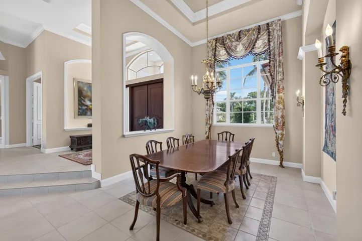 Dining area featuring high ceilings, crown molding, arched architectural wall cutouts, a custom-installed chandelier, and large windows with transom detail