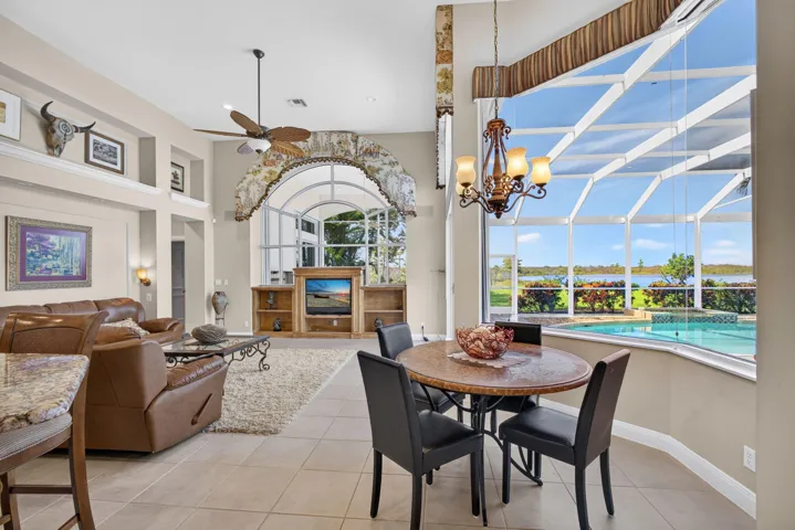 Open-concept interior featuring large-format tile flooring, a custom arched built-in media center, high ceilings with a ceiling fan, and a sprawling window wall enclosure showcasing water frontage and an in-ground pool