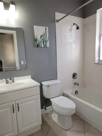 Bathroom featuring a white vanity cabinet, a shower-tub combination with white subway tile surround, a wall-mounted light fixture, and tile flooring