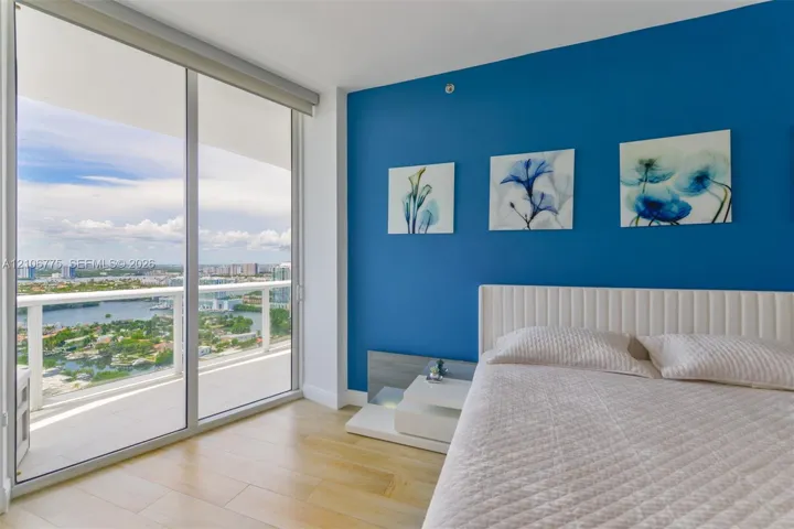 Floor-to-ceiling glass sliding doors opening to a private balcony, wood-finish flooring, and an expansive cityscape backdrop