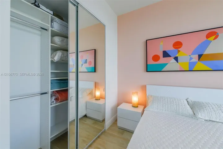 Built-in closet featuring adjustable shelving, hanging rods, and sliding mirrored doors, complemented by wood-finish flooring